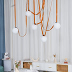 The Clérachic Strap-Hung Glass Globe Pendant Light's orange leather globes staggered over a marble-top console beside a floral arrangement.