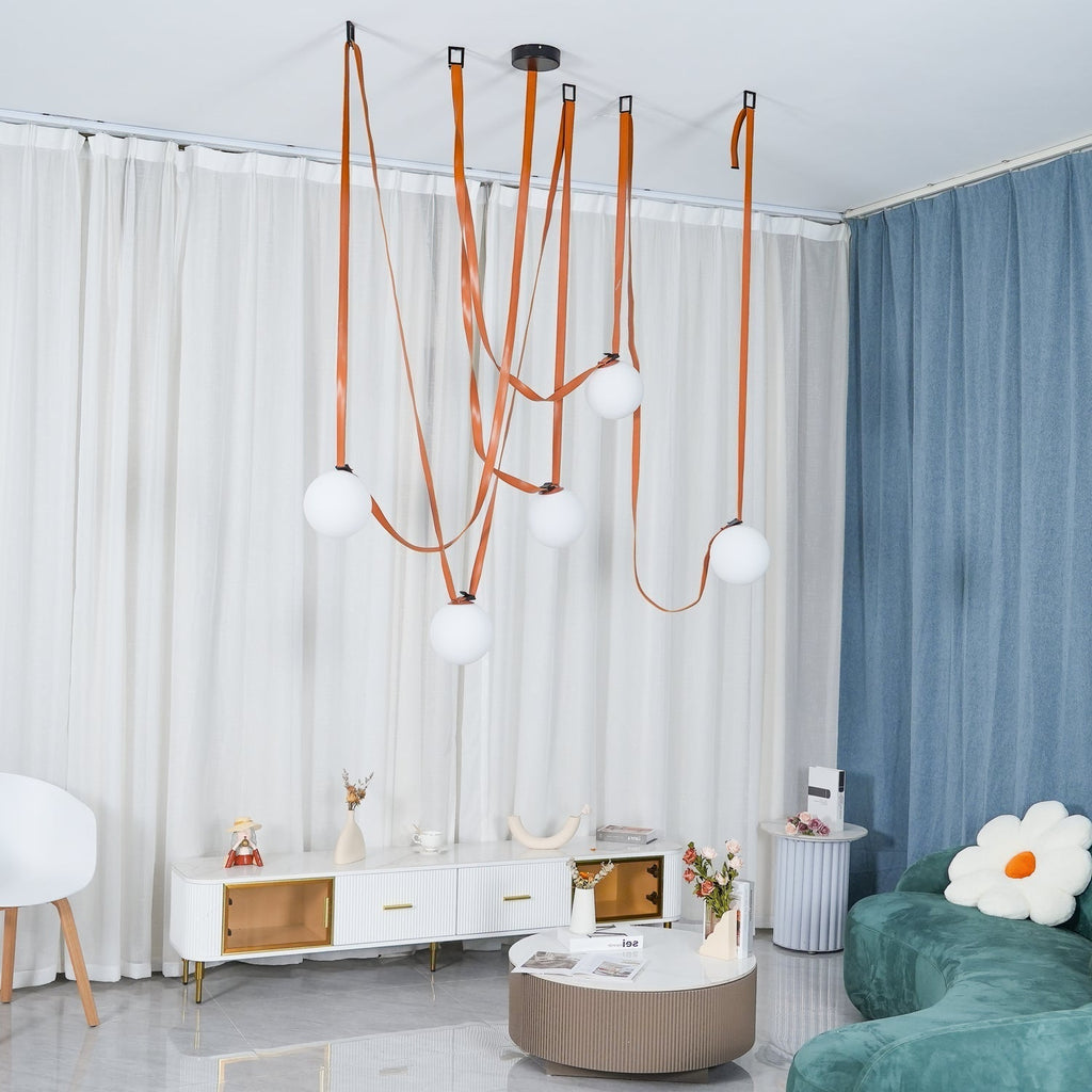 Full-room view of the Clérachic Strap-Hung Glass Globe Pendant Light in leather, globes staggered above a living space with a teal sofa and blue drape.