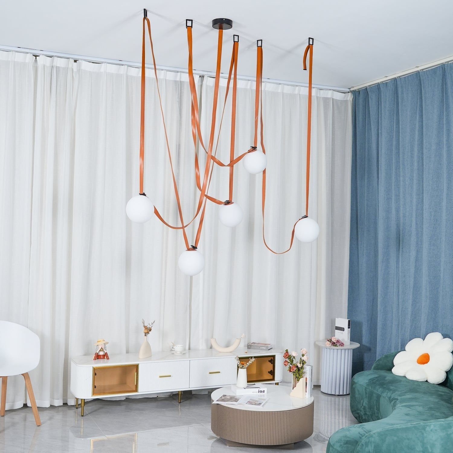 Full-room view of the Clérachic Strap-Hung Glass Globe Pendant Light in leather, globes staggered above a living space with a teal sofa and blue drape.