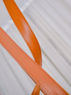 Macro detail of the orange leather strap on the Clérachic Strap-Hung Glass Globe Pendant Light, showing its stitched edge and matte finish.