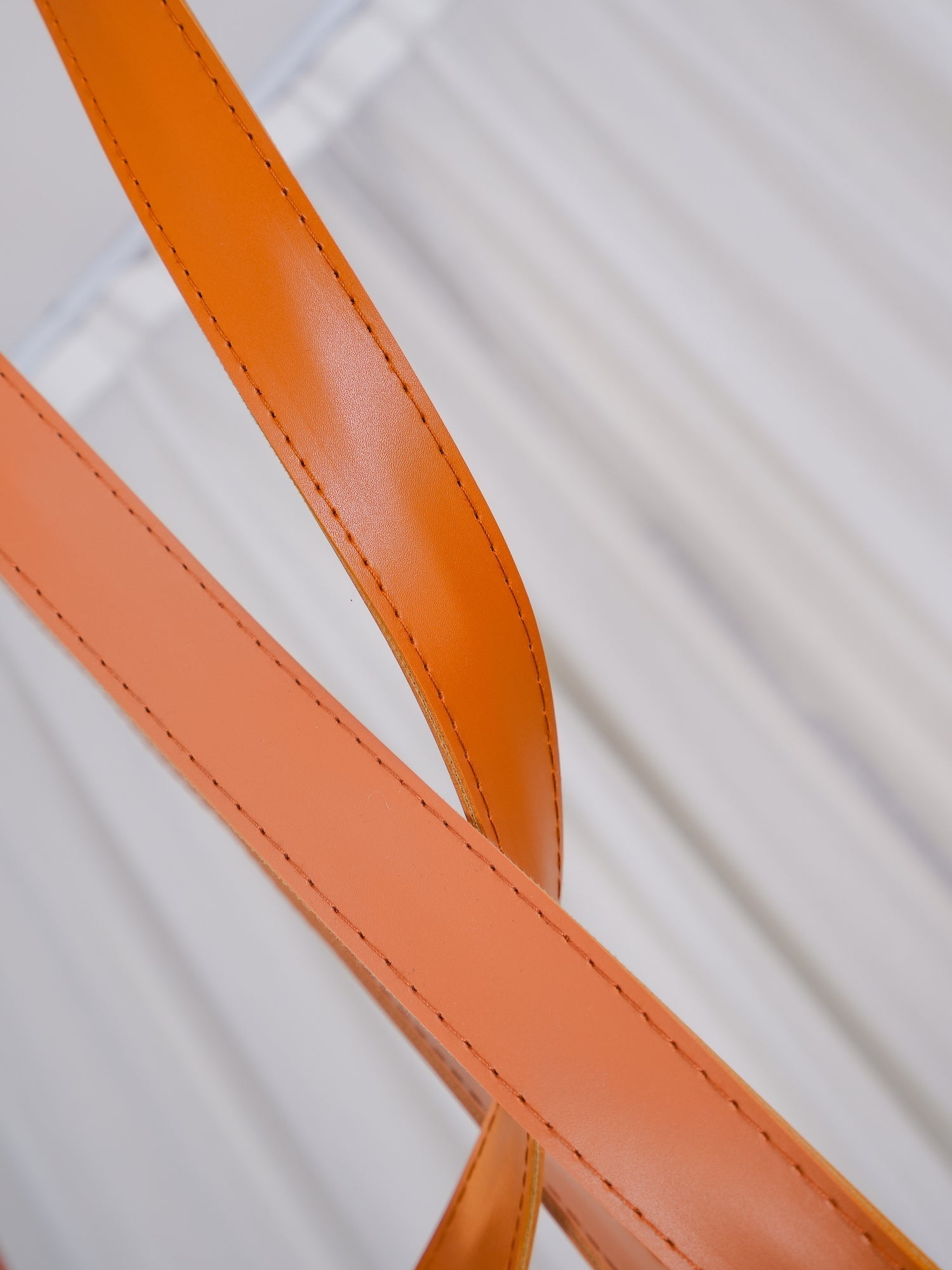 Macro detail of the orange leather strap on the Clérachic Strap-Hung Glass Globe Pendant Light, showing its stitched edge and matte finish.