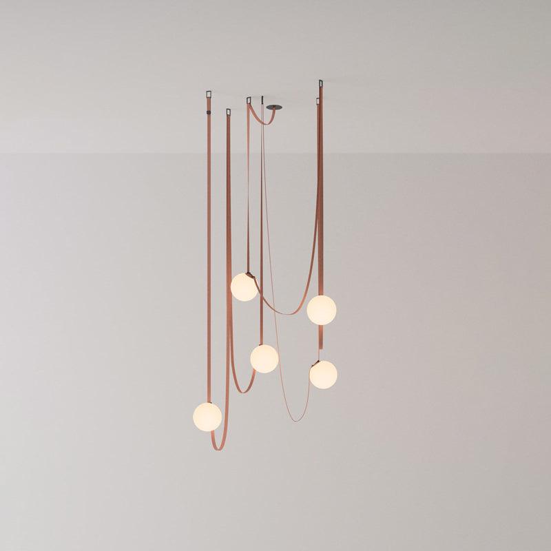 Studio view of the Clérachic Strap-Hung Glass Globe Pendant Light in a rust-toned canvas, its globes staggered at three different drop heights.