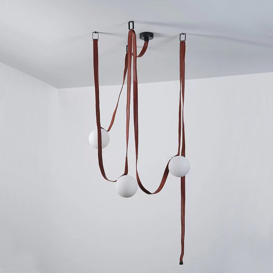 Small vignette of the Clérachic Strap-Hung Glass Globe Pendant Light's three-head version, its brick-red straps looping to globes at different heights.