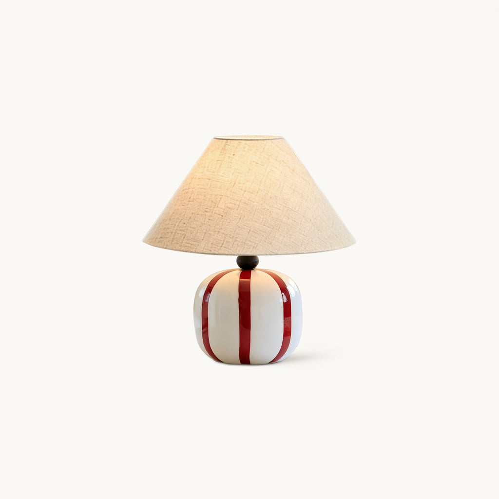 This Clérachic table lamp on a plain white backdrop, with a red and white striped ceramic base and a conical linen shade.