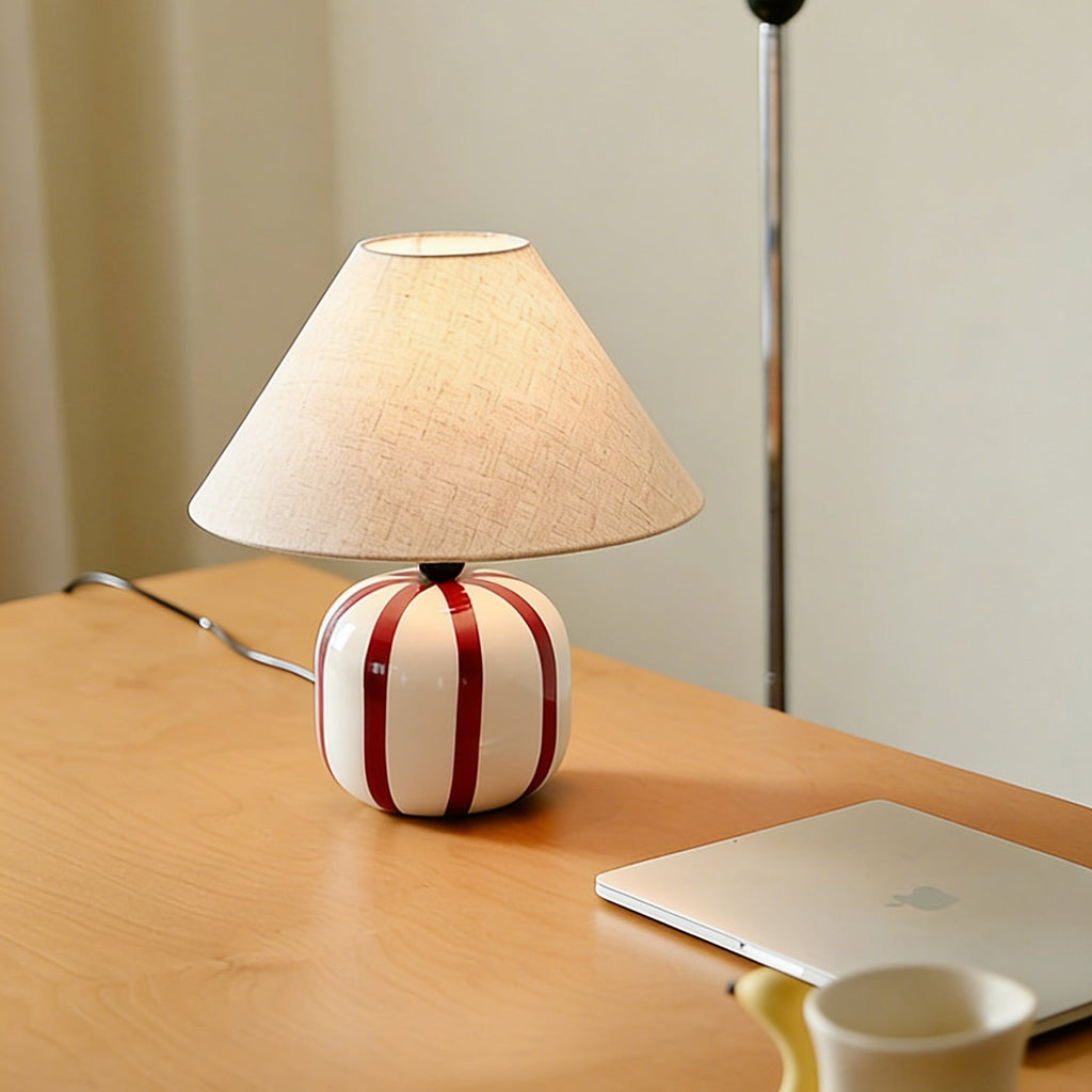 Red and white striped ceramic lamp from Clérachic glowing on a light wood desk, with a laptop and a yellow mug nearby.