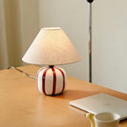 Red and white striped ceramic lamp from Clérachic glowing on a light wood desk, with a laptop and a yellow mug nearby.