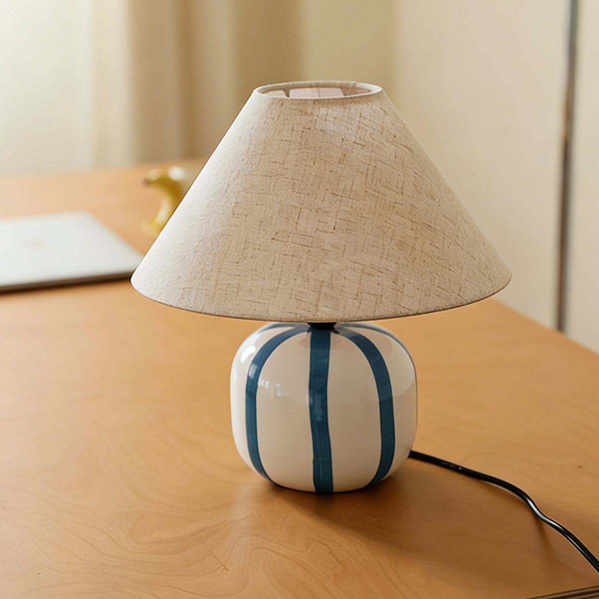 Unlit blue and white striped Clérachic table lamp on a wooden desk, its black cord trailing off to the right.