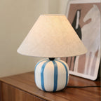 Blue and white striped base of this Clérachic lamp on a dark wood sideboard, with a horse print leaning behind it.