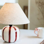 Close view of the red striped ceramic base and linen shade of this Clérachic lamp, with a mug blurred beside it.