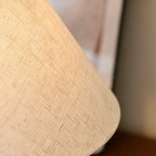 Close view of the woven linen texture on the conical shade of this Clérachic table lamp, softly lit from within.