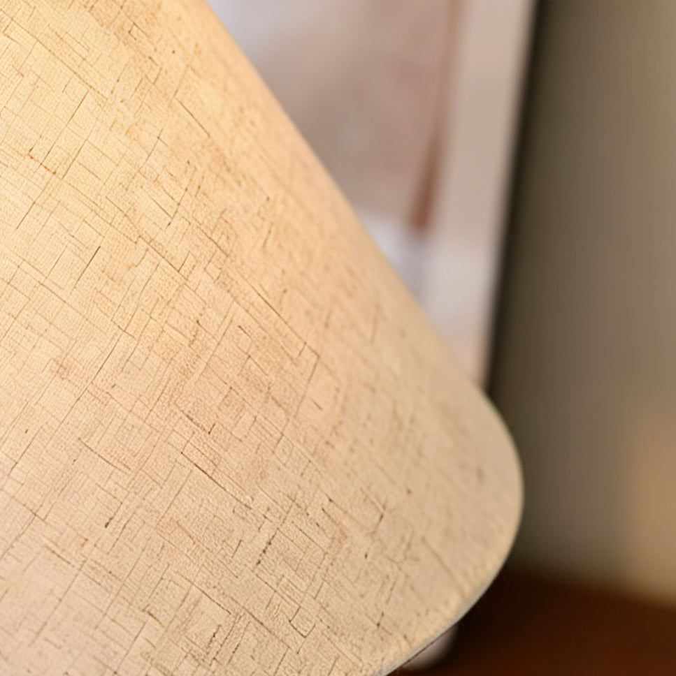 Close view of the woven linen texture on the conical shade of this Clérachic table lamp, softly lit from within.