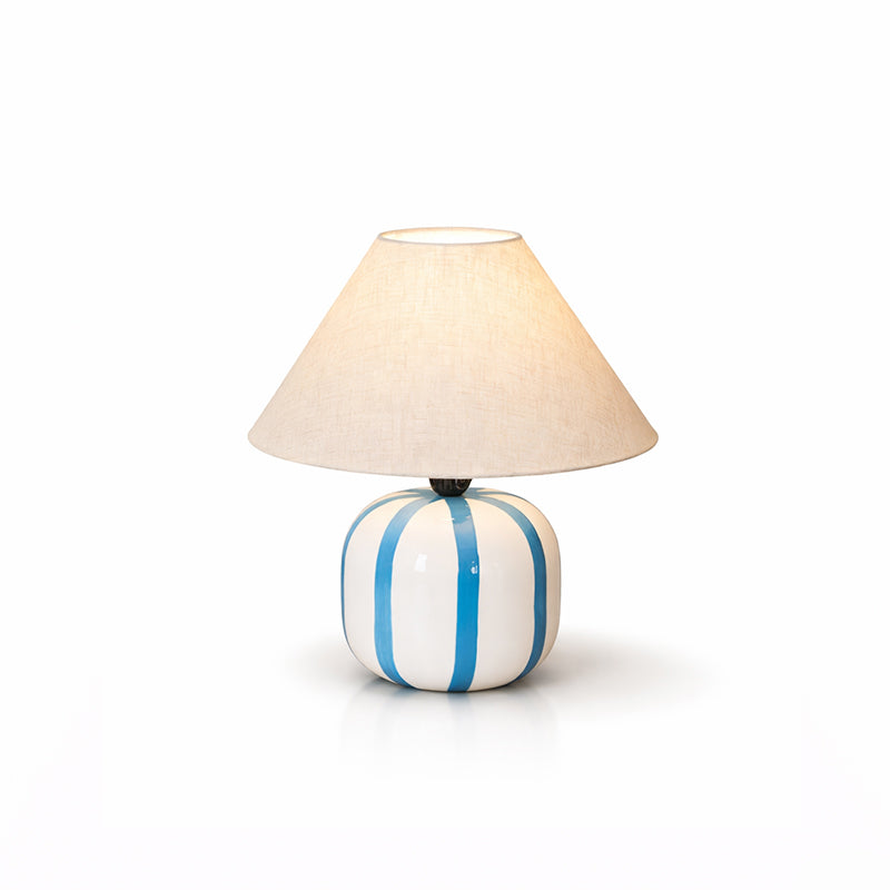 This Clérachic table lamp with blue and white stripes, shown lit on a clean white background with a soft reflection.