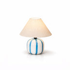 This Clérachic table lamp with blue and white stripes, shown lit on a clean white background with a soft reflection.