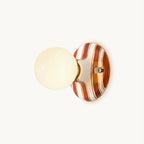 Cut-out view of a Clérachic wall light with a frosted globe and a brown and white striped ceramic backplate, on a plain backdrop.