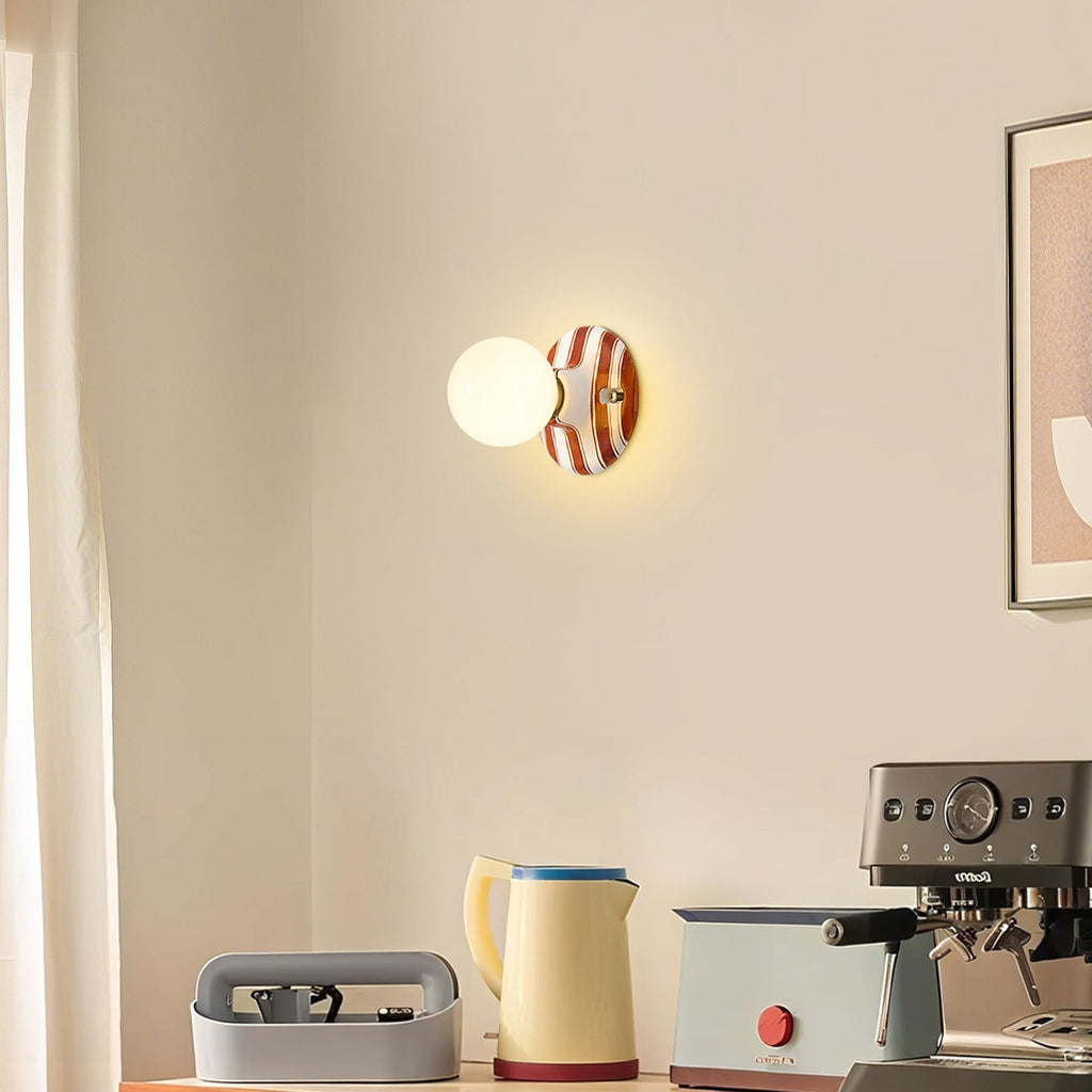 A small Clérachic wall light with a brown and white striped backplate glows on a cream wall above a kettle and espresso machine.