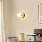 A small Clérachic wall light with a brown and white striped backplate glows on a cream wall above a kettle and espresso machine.