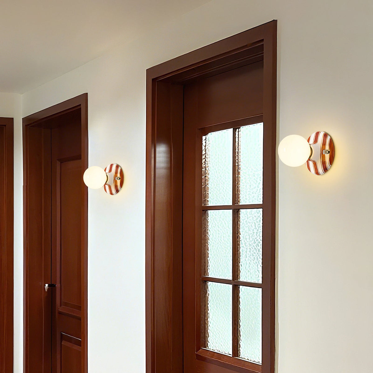 Two Clérachic wall lights with frosted globes and brown and white striped backplates, mounted beside dark wooden doors in a hallway.