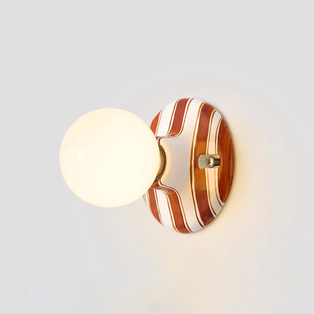 Lit frosted globe on a brown and white striped ceramic backplate, this Clérachic wall light against a pale grey wall.