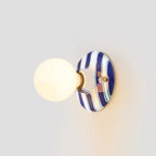 Blue and white striped ceramic backplate and lit frosted globe on a Clérachic wall light, seen from slightly to the side on grey.