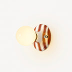 Frosted globe glowing on a brown and white striped ceramic backplate, this Clérachic wall light on a pale wall.