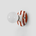 Unlit clear-looking glass globe on a brown and white striped ceramic backplate, this Clérachic wall light on a grey wall.