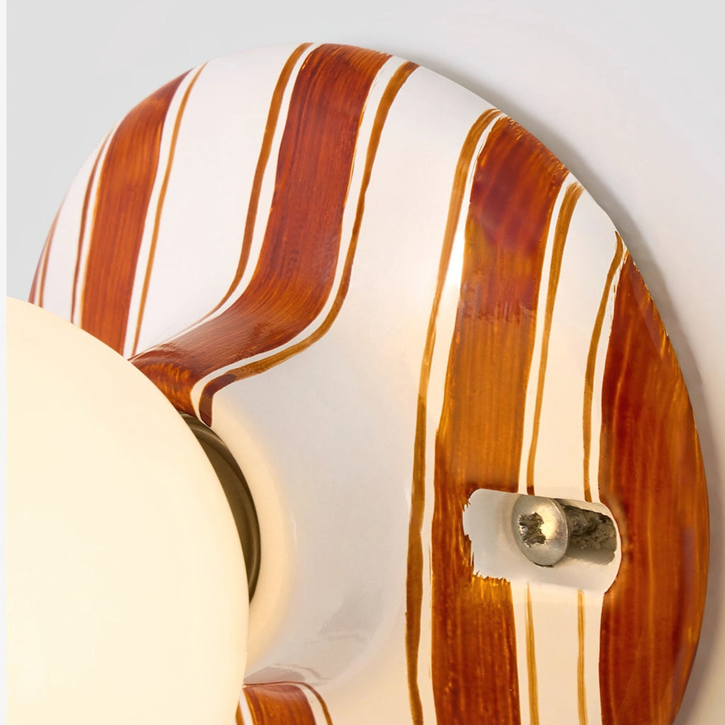 Close view of the hand-painted brown and white stripes and the brass screw on the ceramic backplate of this Clérachic wall light.