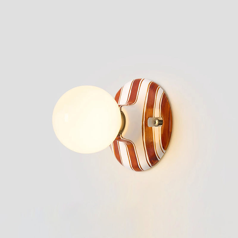 Side view of this Clérachic wall light, a lit frosted globe on a rounded brown and white striped backplate with a soft shadow.