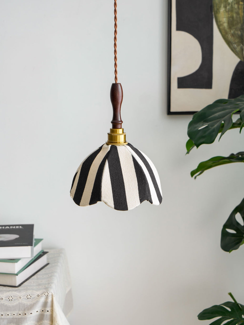 Black-and-cream fabric pendant with a wooden finial hung beside a framed abstract print and a monstera leaf, from Clérachic.