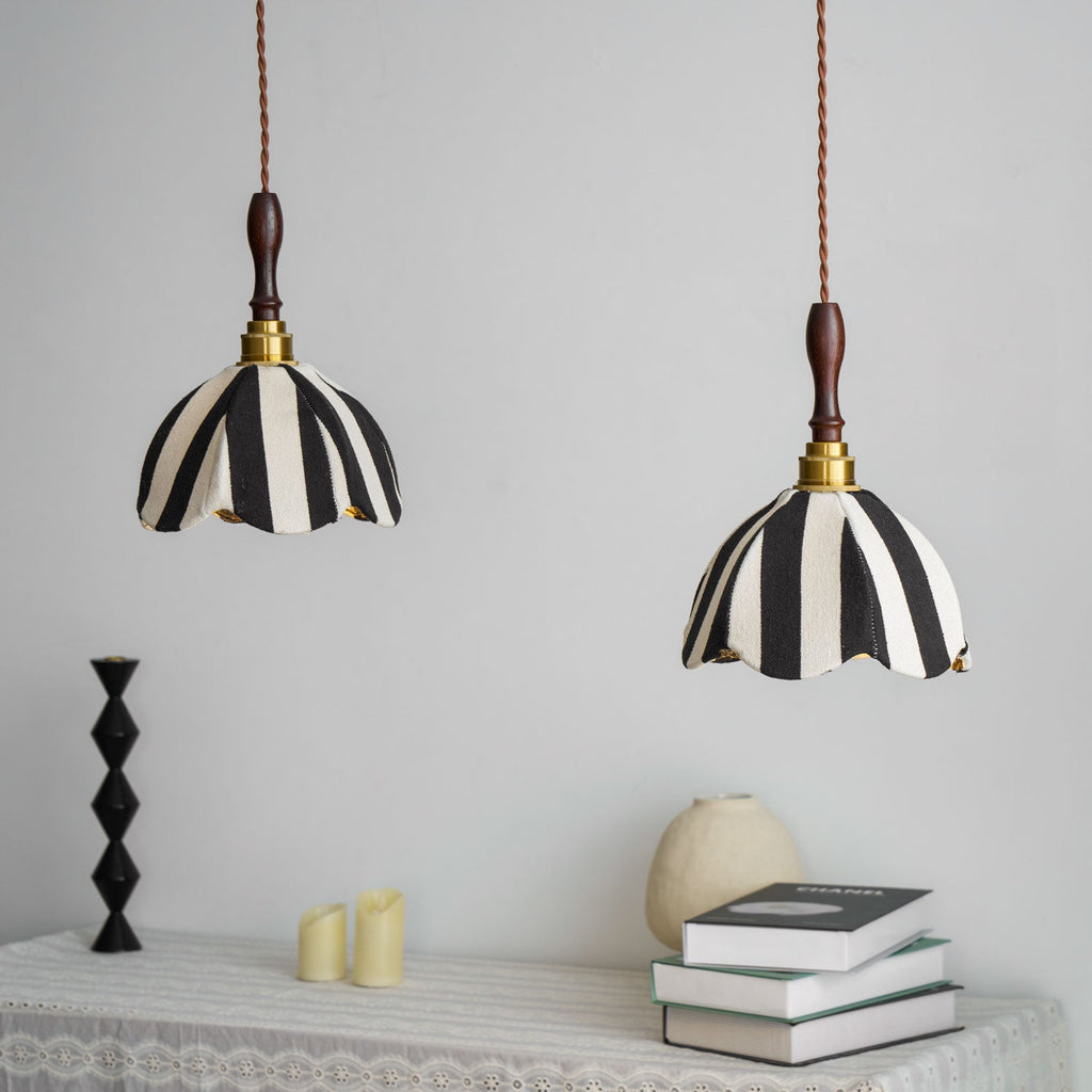 Two Clérachic striped fabric pendants hang above a lace-covered table with books, a pale vase and a black candlestick.