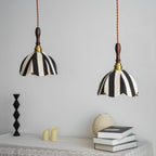 Two Clérachic striped fabric pendants hang above a lace-covered table with books, a pale vase and a black candlestick.