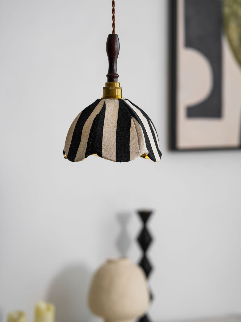 Soft-focus view of this Clérachic striped pendant against a grey wall, with a framed print and ceramic vases behind it.