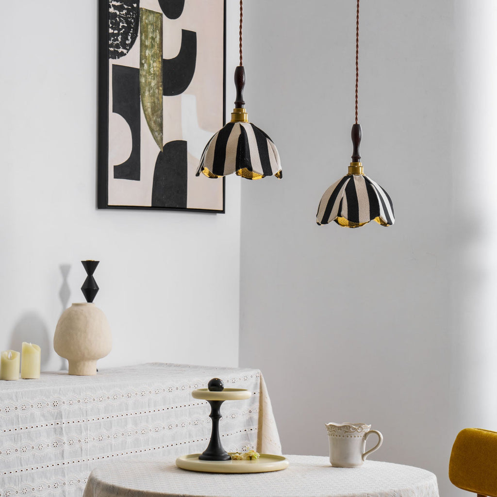 Two small striped pendants with wood finials hang near a round table set with a cup and a cake stand, from Clérachic.
