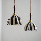 Two black-and-cream fabric pendants at different heights against a pale wall, brass collars catching the light, from Clérachic.