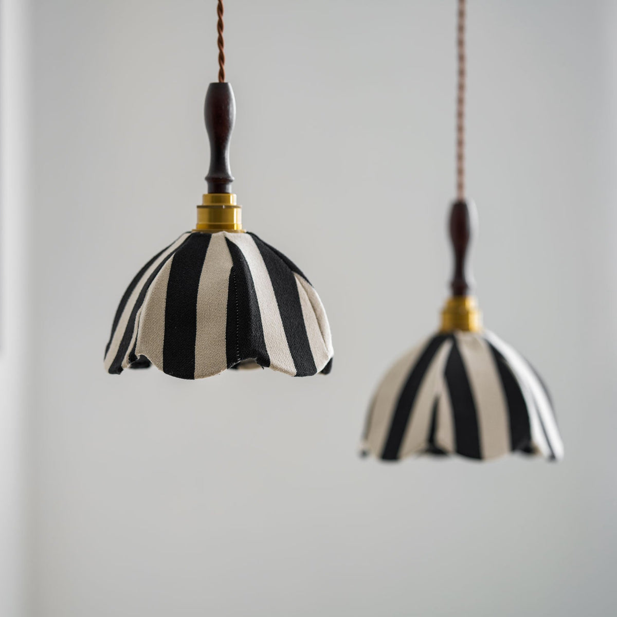 Two black-and-cream fabric pendants at different heights against a pale wall, brass collars catching the light, from Clérachic.