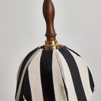 Close view of the knitted black-and-cream stripes, brass collar and turned wood finial on this Clérachic pendant.