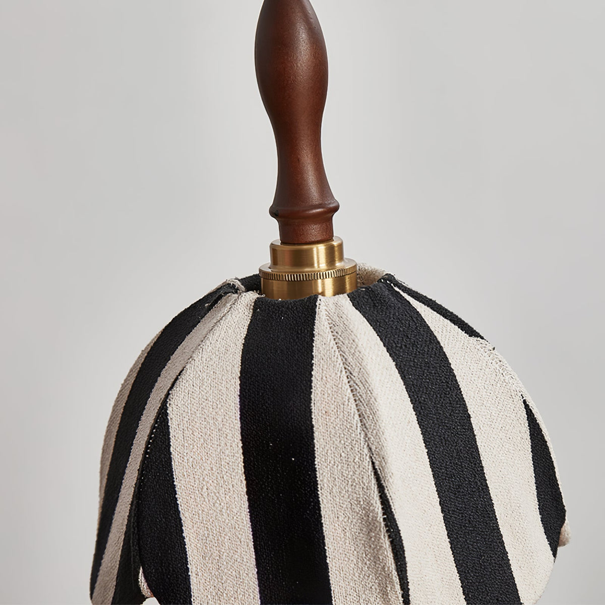 Close view of the knitted black-and-cream stripes, brass collar and turned wood finial on this Clérachic pendant.