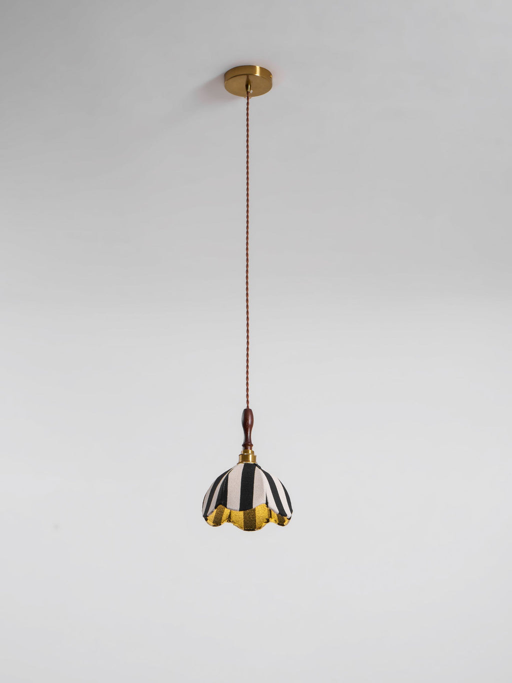 This Clérachic striped pendant hangs from a round brass ceiling canopy on a long brown twisted cord against a grey wall.