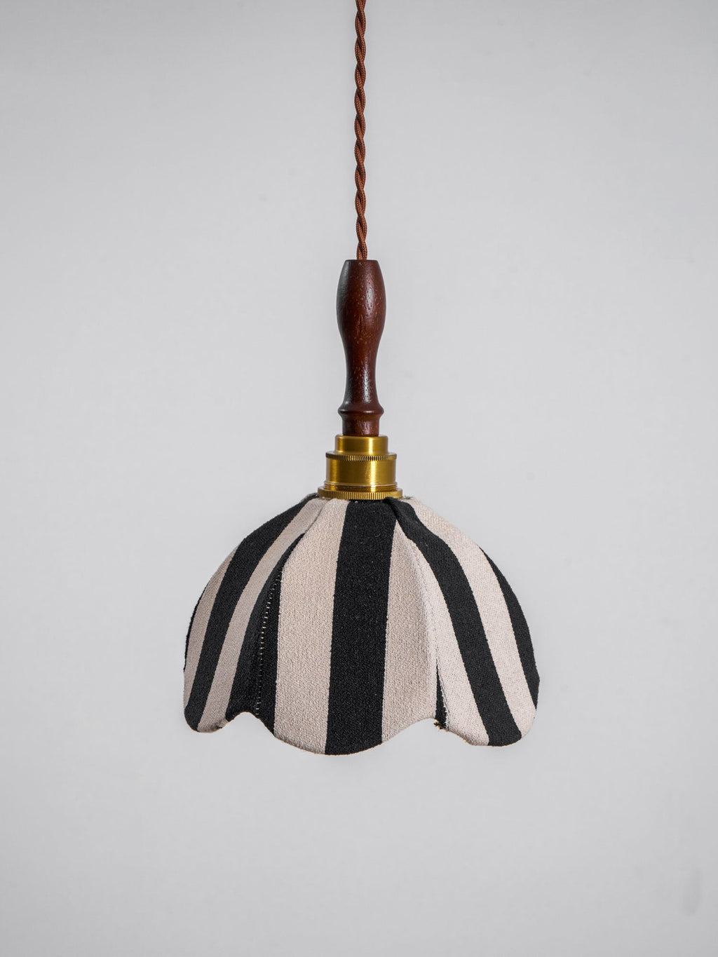 Black-and-cream fabric pendant with a scalloped edge, a brass socket and a polished wood finial, on a plain grey backdrop, from Clérachic.
