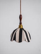 Black-and-cream fabric pendant with a scalloped edge, a brass socket and a polished wood finial, on a plain grey backdrop, from Clérachic.