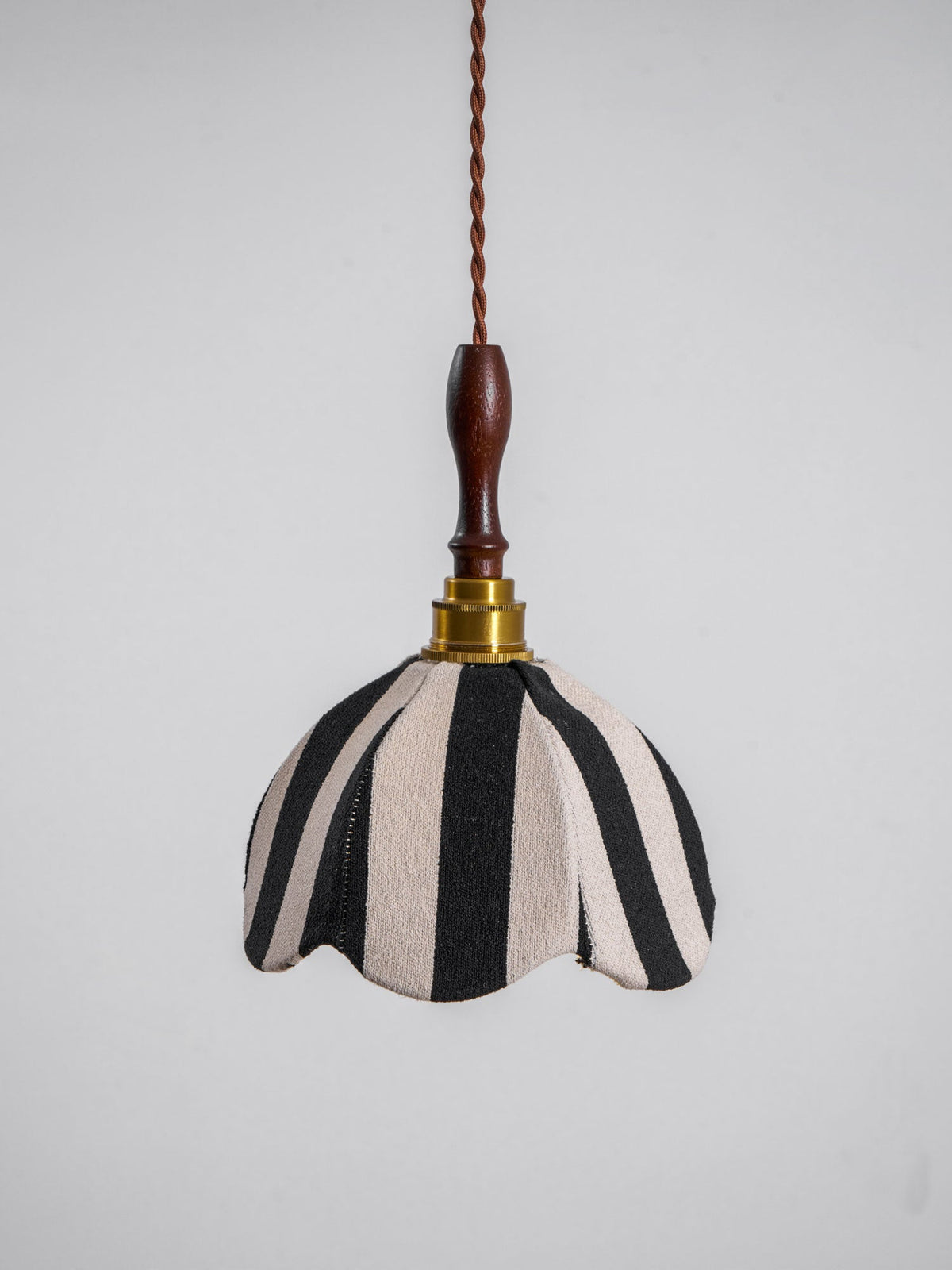 Black-and-cream fabric pendant with a scalloped edge, a brass socket and a polished wood finial, on a plain grey backdrop, from Clérachic.