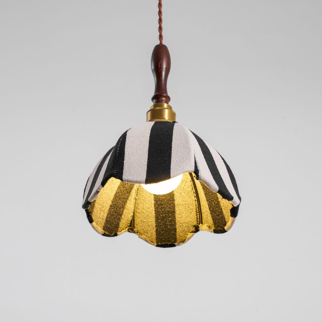Lit Clérachic striped pendant seen from below, the bulb glowing and the gold lining showing inside the scalloped hem.