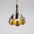 Lit Clérachic striped pendant seen from below, the bulb glowing and the gold lining showing inside the scalloped hem.
