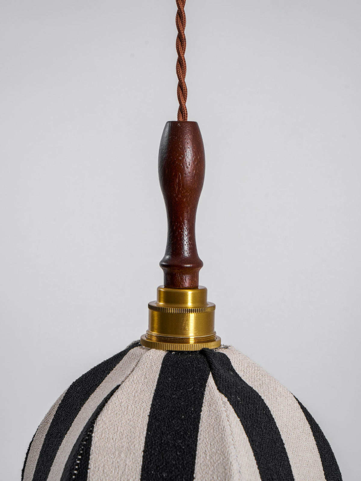Close view of the brass collar and dark wood finial joining the twisted cord to the striped shade on this Clérachic pendant.
