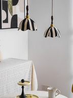 Two striped pendants hang over a corner table with a lace cloth and a teacup, a pair of Clérachic lamps beside a framed print.