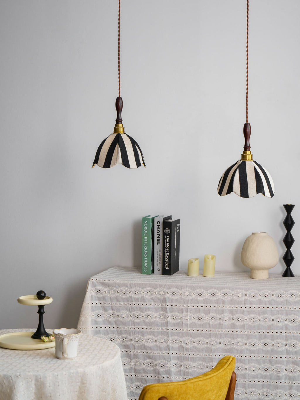 Pair of striped fabric pendants above a lace-covered table with books and candles, a yellow chair nearby, from Clérachic.