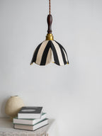 Black-and-cream Clérachic fabric pendant hung above a stack of books and a round stone-coloured vase against a pale wall.