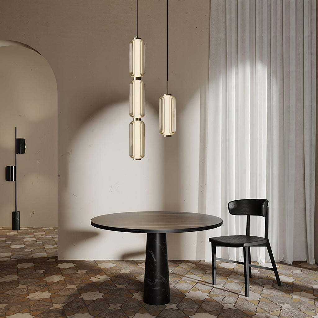 Two Clérachic ribbed glass pendants, one in three tiers, hang over a round dark table and a black chair on a tiled floor.