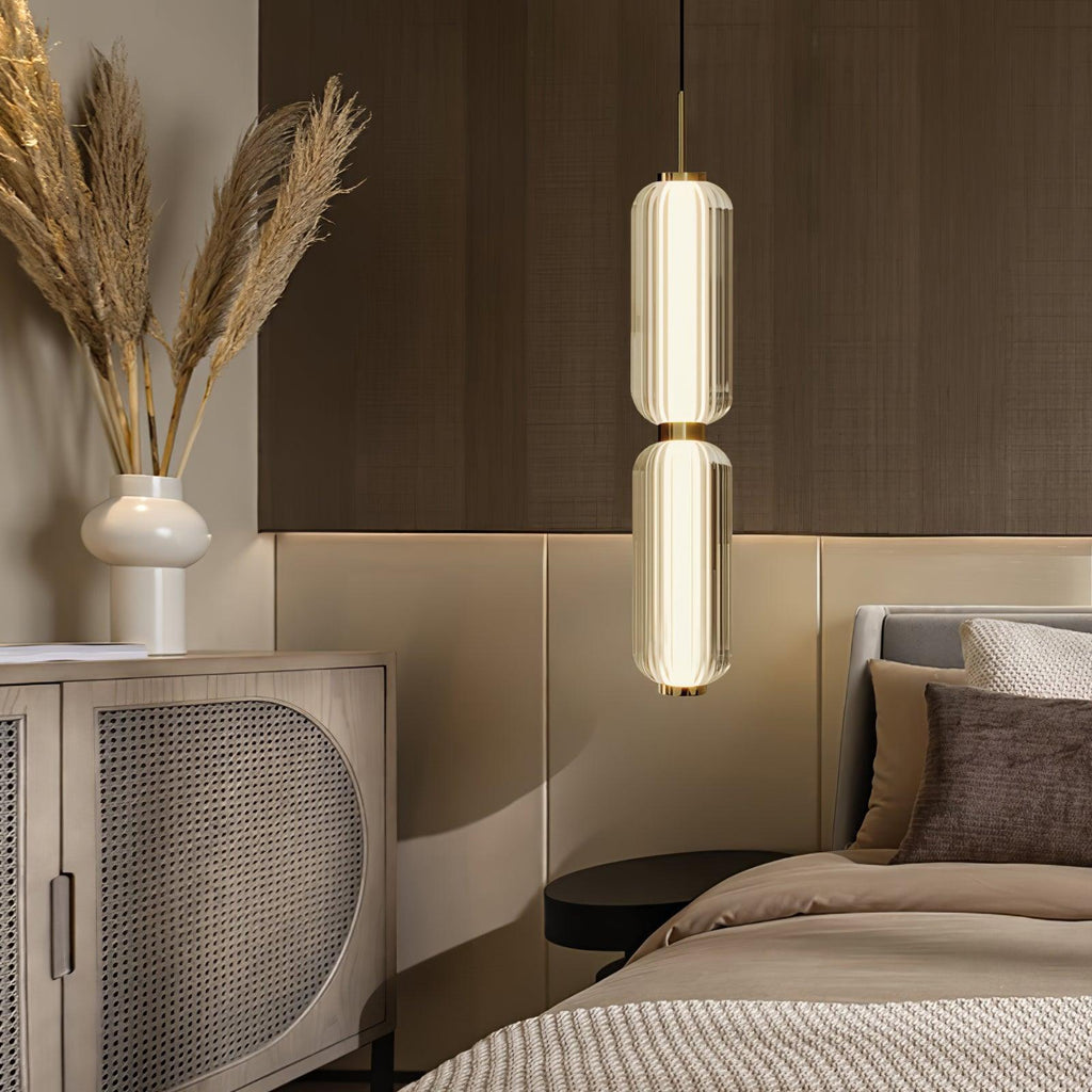A two-tier ribbed glass Clérachic pendant lit above a bedside, with pampas grass in a cream vase and a rattan cabinet.