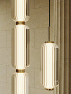 Close view of ribbed glass tiers and gold collars on two Clérachic pendants, against a stone-textured wall and curtain.