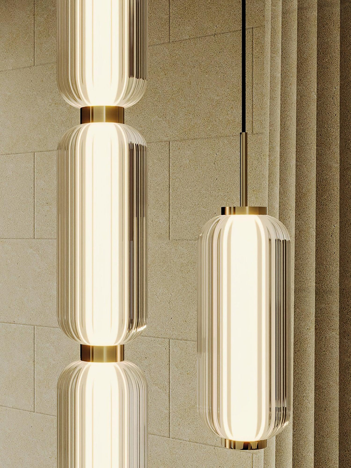 Close view of ribbed glass tiers and gold collars on two Clérachic pendants, against a stone-textured wall and curtain.